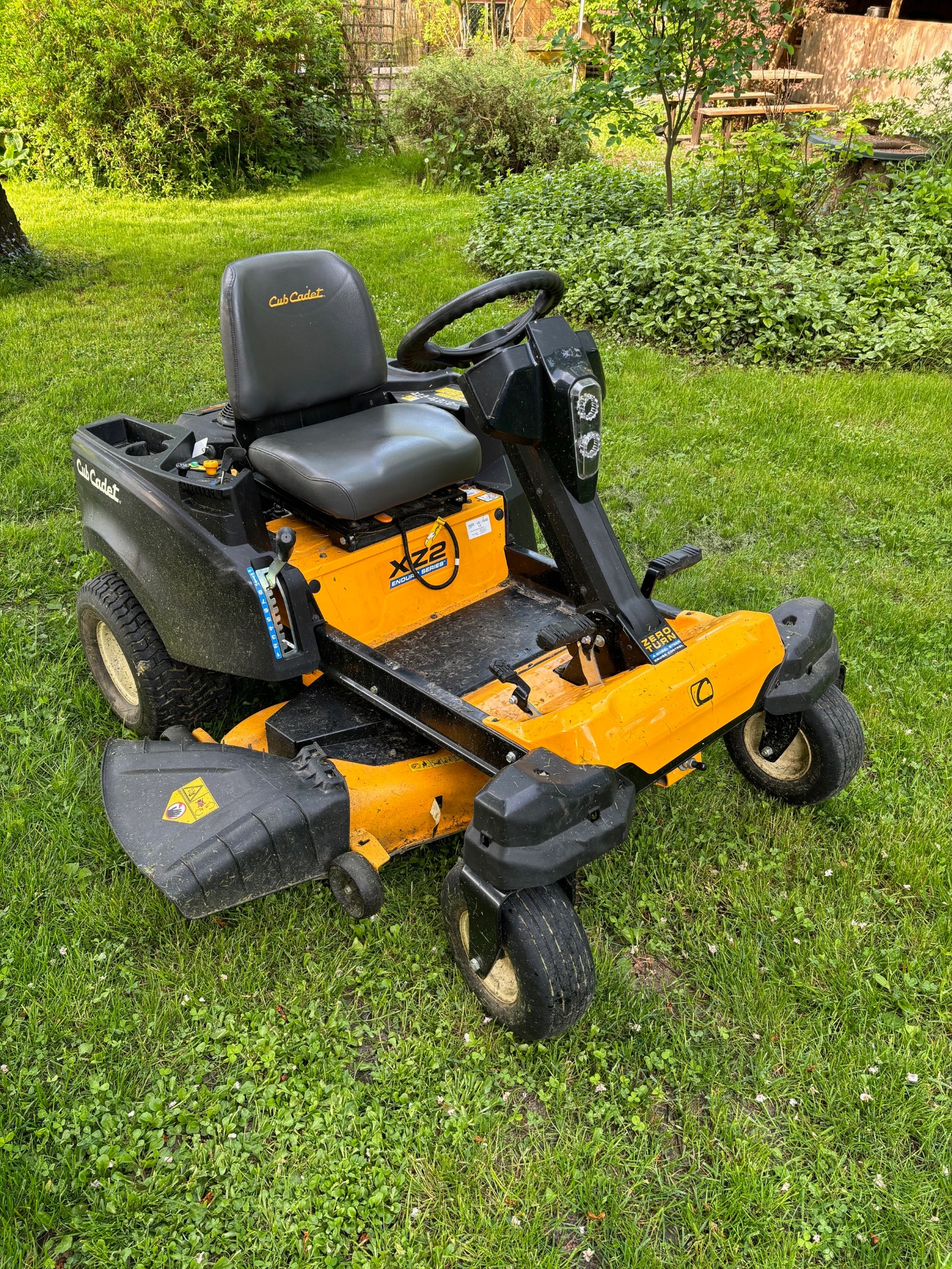 Żółto-czarna kosiarka samojezdna Cub Cadet XZ2 na trawniku z koniczyną, otoczona zielenią. Widoczne szczegóły konstrukcji i oznaczenia modelu.