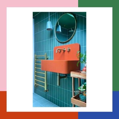 Pomarańczowa umywalka z baterią w stylu retro na tle turkusowych płytek, okrągłe lustro i grzejnik drabinkowy w nowoczesnej łazience.