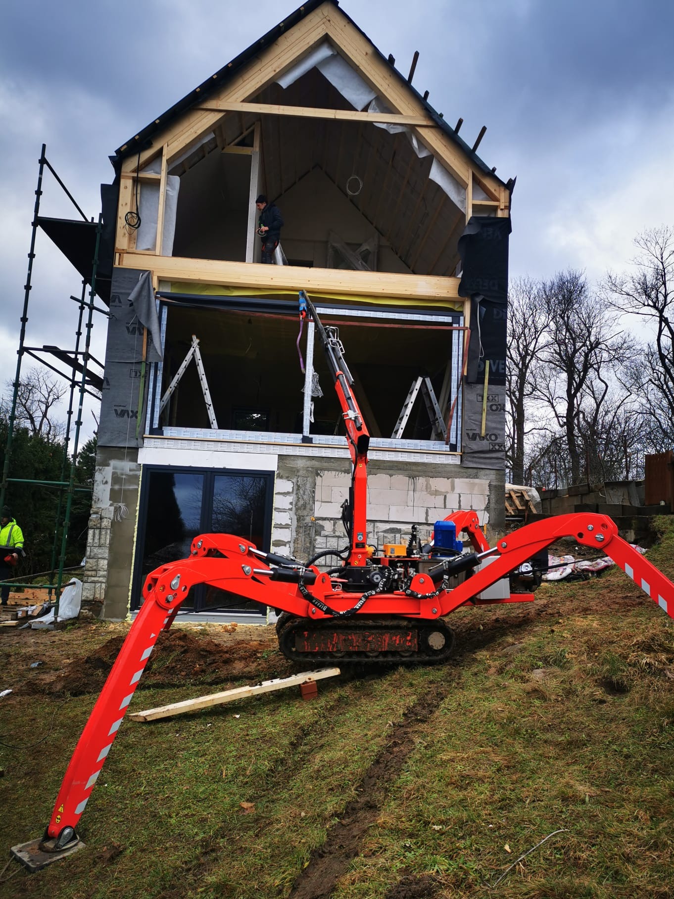 Montaż okna w surowym stanie budynku jednorodzinnego z użyciem czerwonego minikoparki z przyssawkami do szyb.