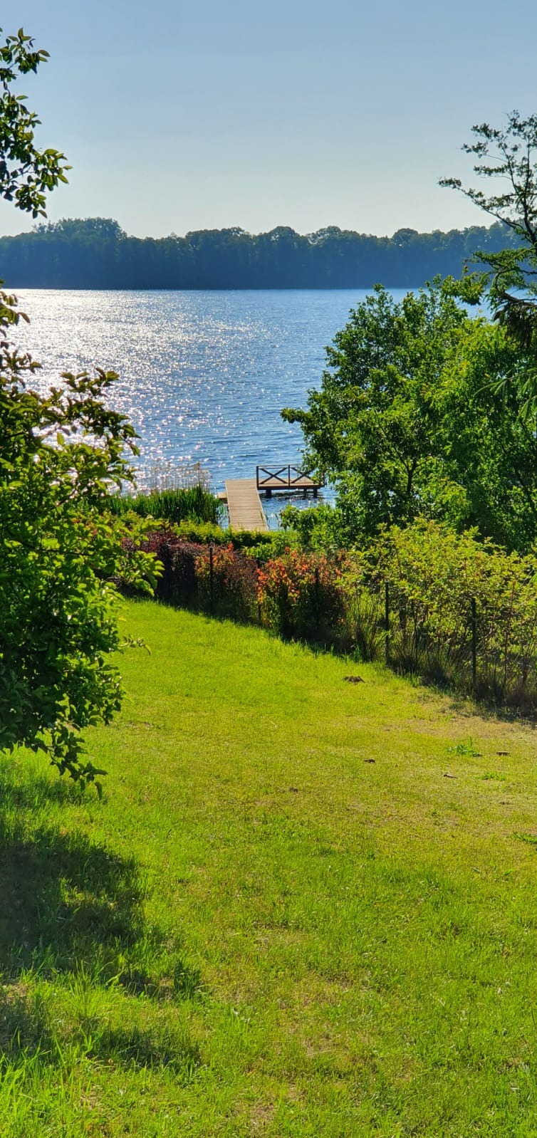 Malowniczy widok na jezioro z drewnianym pomostem w Santoku, otoczony zielenią drzew i krzewów.