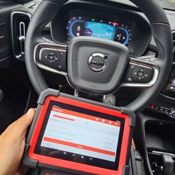 AUTO-INSPEKCJA.PL - Wnętrze samochodu Volvo XC40 z tabletem diagnostycznym marki Launch na desce rozdzielczej, wyświetlającym raport o stanie systemów pojazdu podczas skanowania. Na przedniej szybie widoczne krople...