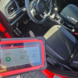 AUTO-INSPEKCJA.PL - Wnętrze czerwonego samochodu Volkswagen T-Roc sfotografowane z perspektywy pierwszej osoby podczas diagnostyki komputerowej z użyciem tabletu diagnostycznego, pokazującego proces łączenia z VCI...