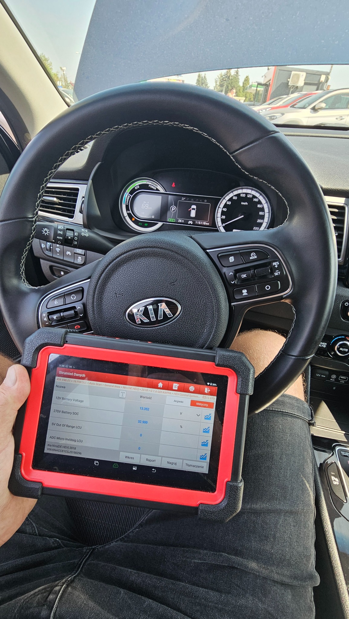 Diagnostyka komputerowa pojazdu marki Kia Niro, odczyt danych z tabletu diagnostycznego na tle kierownicy i deski rozdzielczej.