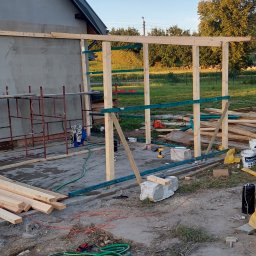 Team-Lewy - Wznoszenie drewnianej konstrukcji z belek na zewnątrz budynku, widoczne rusztowanie, narzędzia i materiały budowlane.