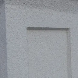 Fragment szarej ściany zewnętrznej z fakturą baranka i wklęsłym, prostokątnym elementem dekoracyjnym.