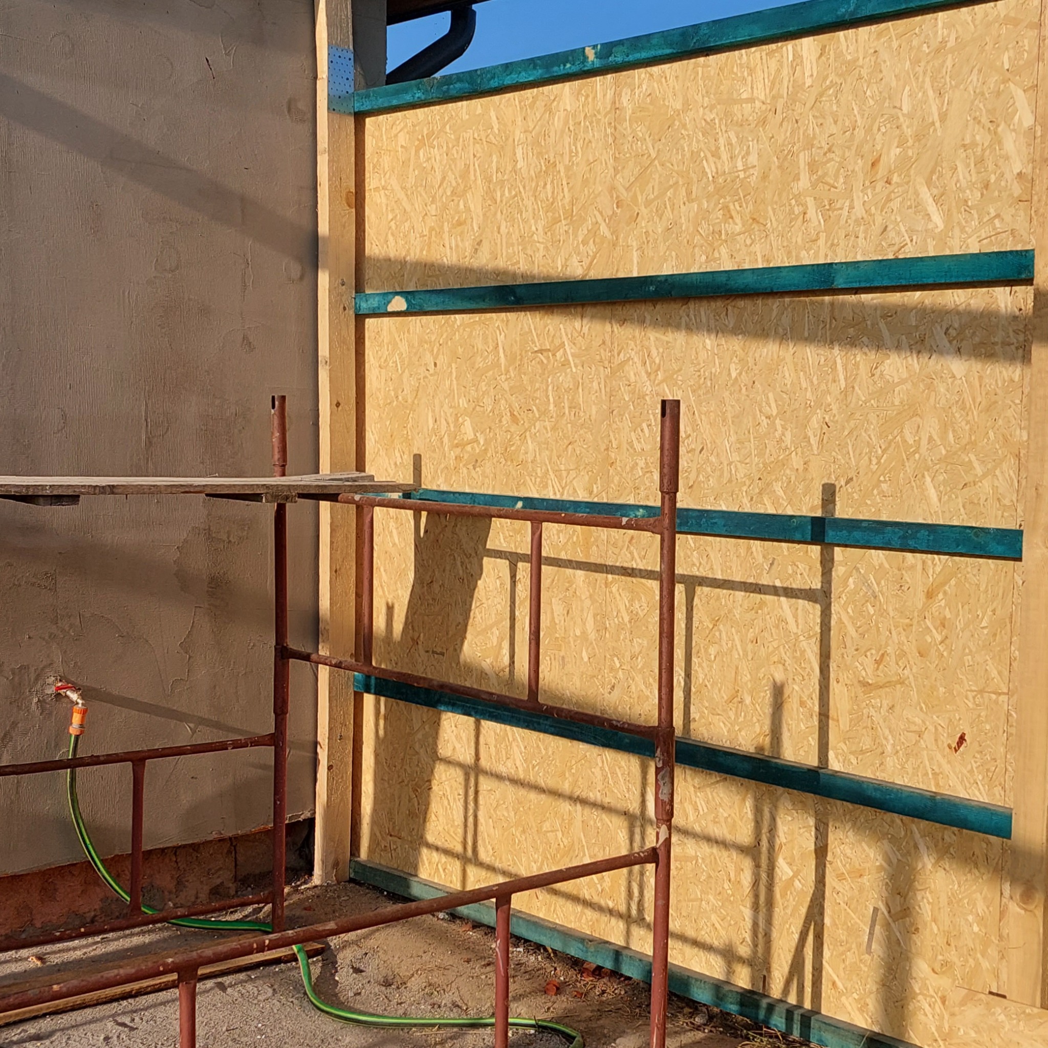 Wnętrze w trakcie ocieplania w Lęborku: ściana z płyty OSB z zielonymi listwami, widoczne rusztowanie i fragment otynkowanej ściany.