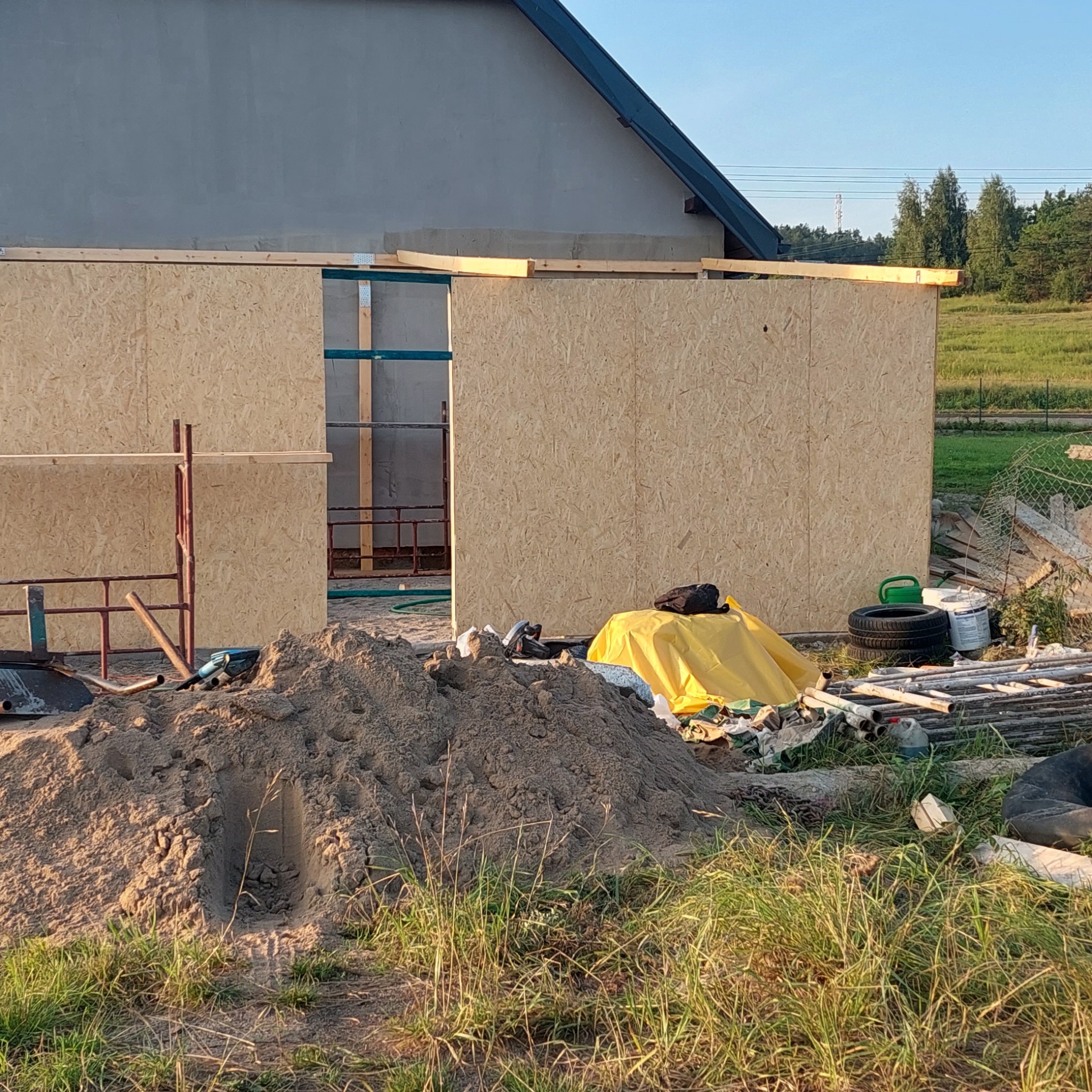 Budowa szkieletu domu z płyt OSB, widoczne drewniane belki konstrukcyjne i sterta piasku na pierwszym planie.