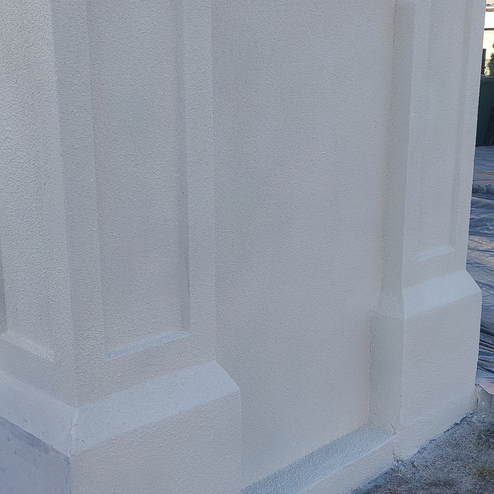 Fragment ocieplonej elewacji budynku z wyraźną strukturą baranka i dekoracyjnymi elementami architektonicznymi, widoczne ślady po pracach wykończeniowych u podstawy.