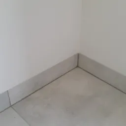 Szare płytki podłogowe i przypodłogowe w rogu pomieszczenia, minimalistyczny design, fuga w kolorze grafitowym.