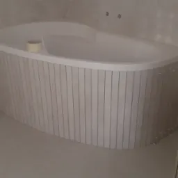 Obudowa wanny z pionowych płytek w trakcie montażu, widoczne krzyżyki dystansowe, rolka taśmy malarskiej na wannie.