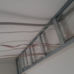 DOM SERWIS Krzysztof Chodorowski - Metalowy stelaż podwieszanego sufitu z płyt kartonowo-gipsowych, z widocznymi przewodami elektrycznymi i peszlem, montowany do stropu.