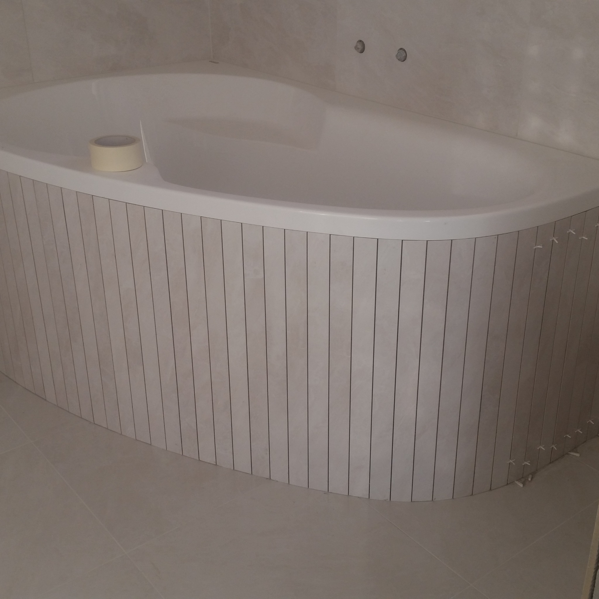 Obudowa wanny z pionowych płytek w trakcie montażu, widoczne krzyżyki dystansowe, rolka taśmy malarskiej na wannie.