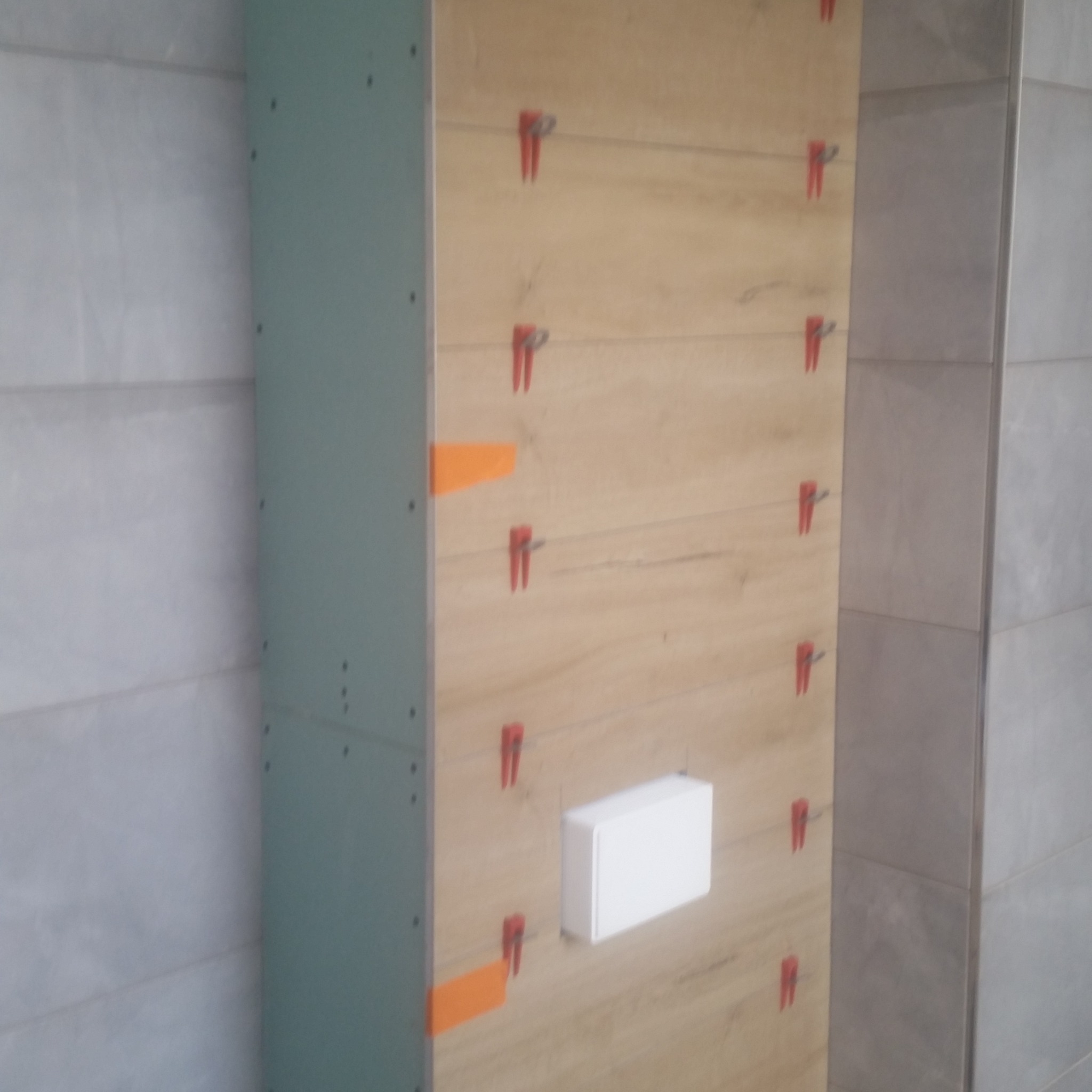 Montaż płytek imitujących drewno na ścianie w łazience, z użyciem klipsów poziomujących i elementów z płyty karton gips.