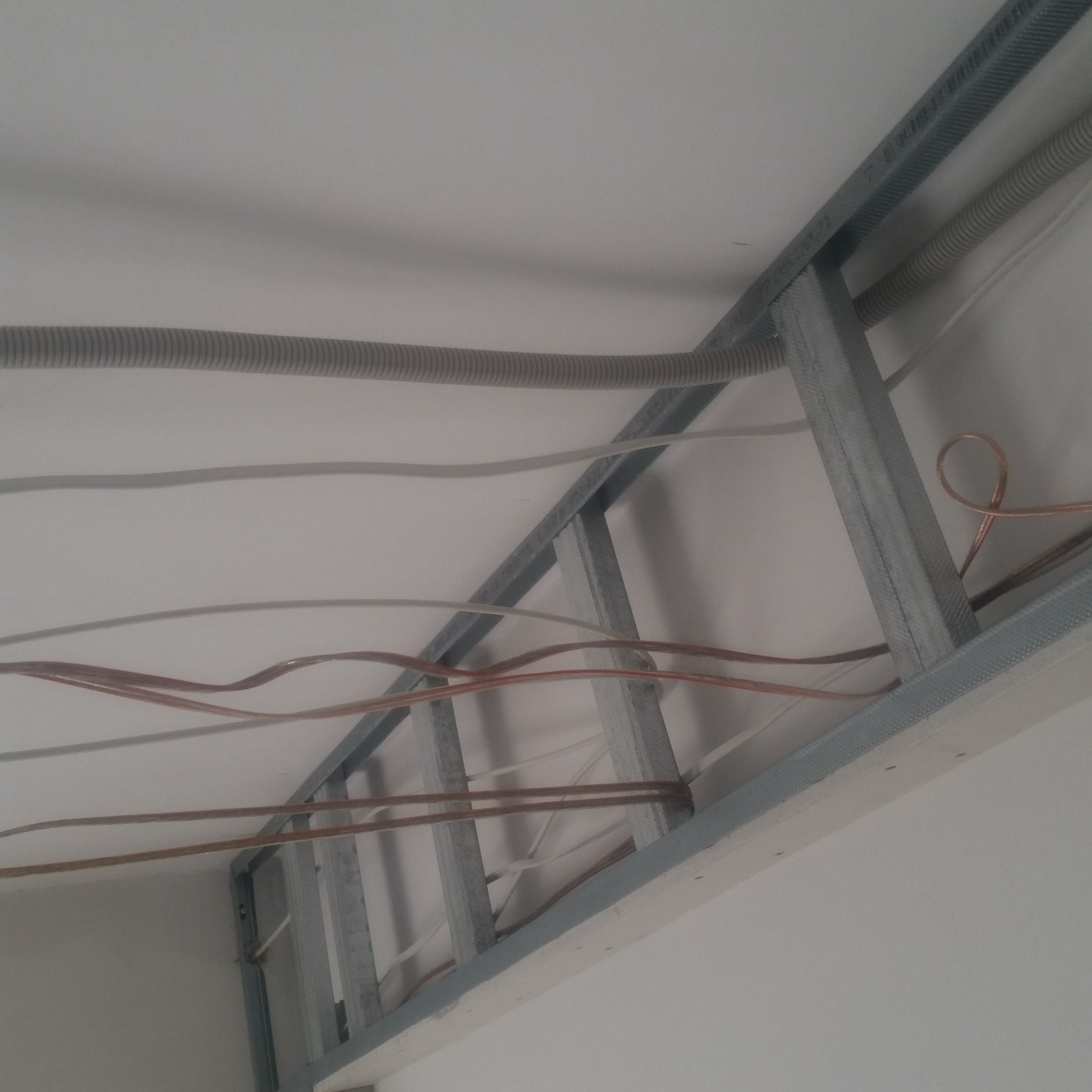Metalowy stelaż podwieszanego sufitu z płyt kartonowo-gipsowych, z widocznymi przewodami elektrycznymi i peszlem, montowany do stropu.