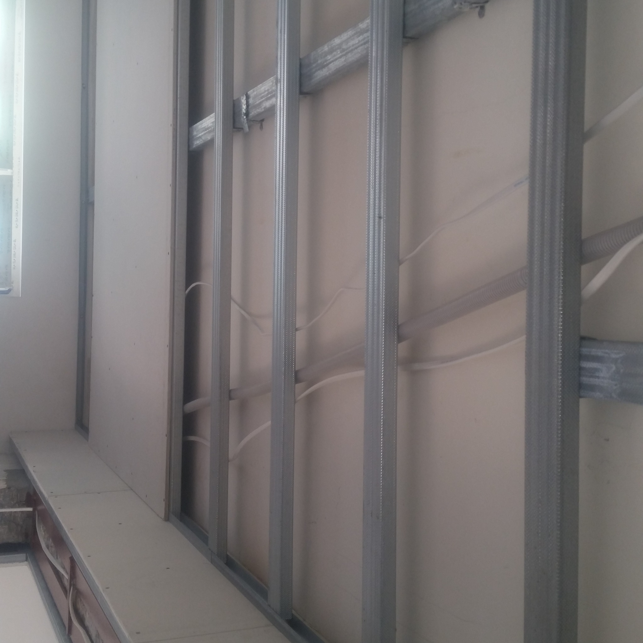 Montaż płyty karton gips na metalowej konstrukcji, widoczne przewody elektryczne w ścianie, częściowo zamontowane płyty.