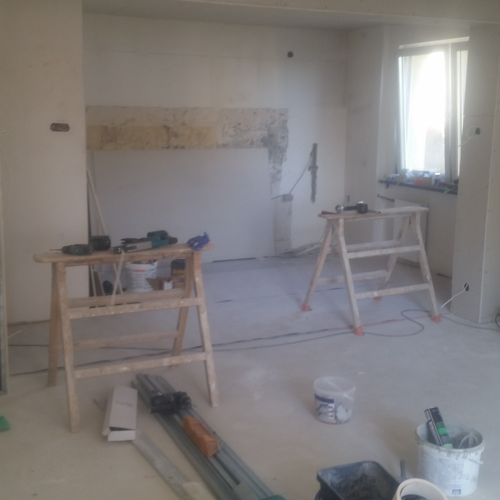 Wnętrze w trakcie prac wykończeniowych w Lubinie: widoczne rusztowania, narzędzia, ślady po skuciu tynku na ścianie i przygotowania do dalszych prac.