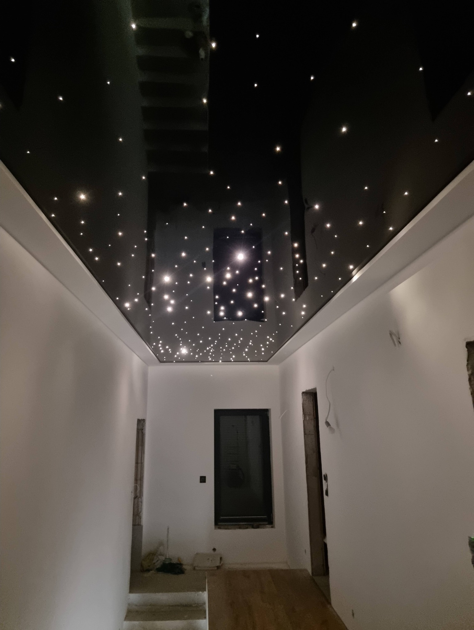 Błyszczący, czarny sufit z efektem gwiazd w białym korytarzu podczas remontu.