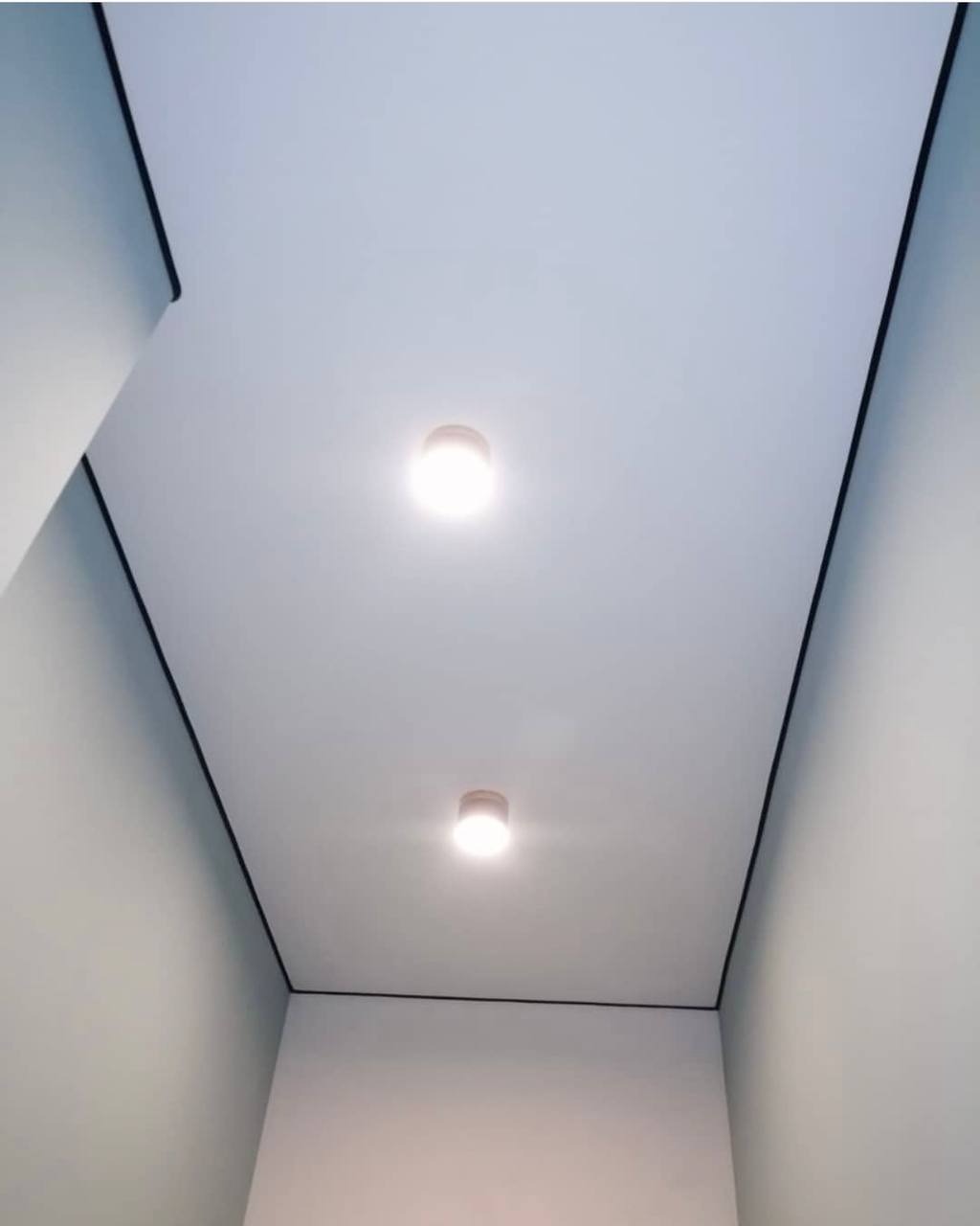 Nowoczesny, biały sufit podwieszany z dwoma punktowymi lampami LED, wykończony czarną listwą dekoracyjną, zrealizowany w mieszkaniu w Poznaniu.