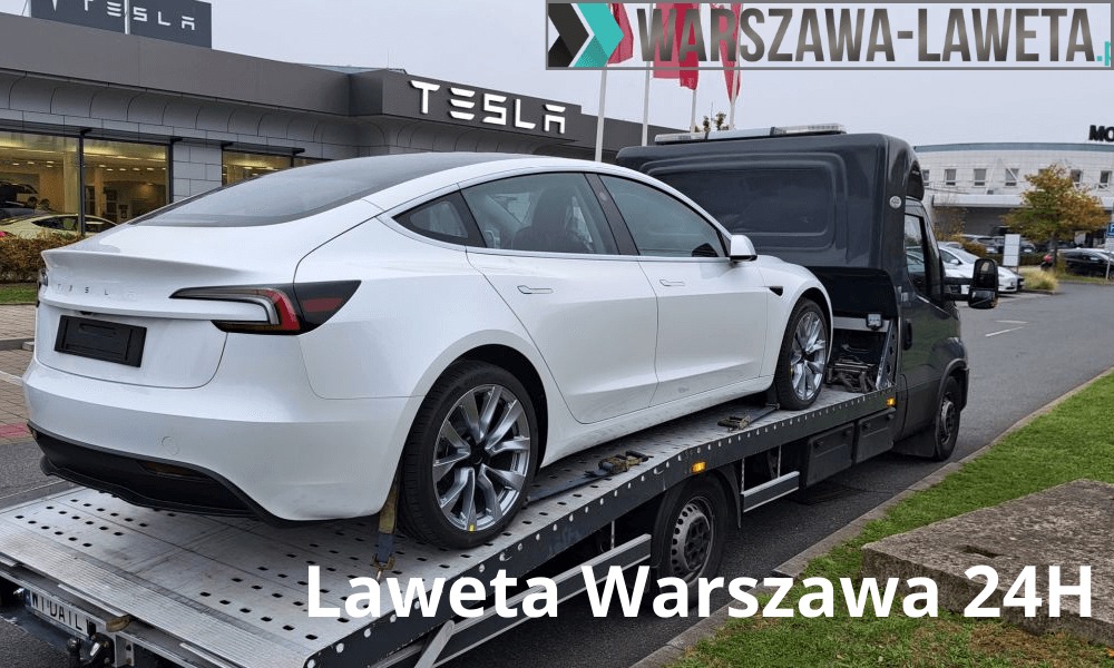 Biała Tesla Model 3 na platformie lawety przed salonem Tesla z widocznym logo firmy na budynku.