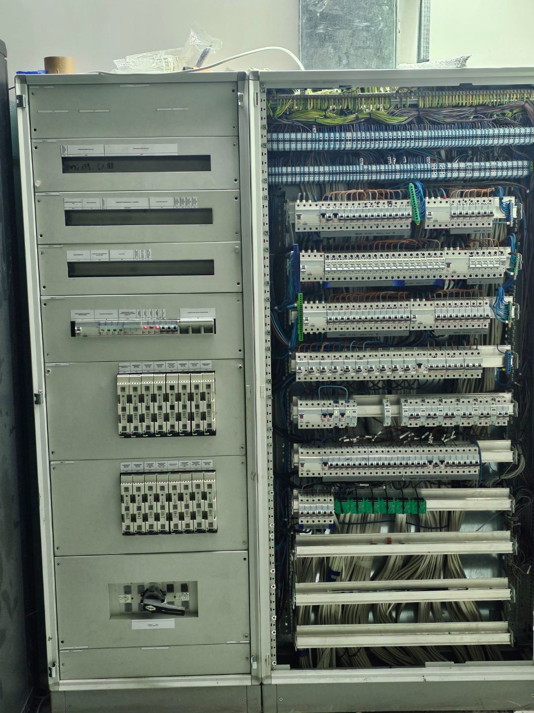 Rozdzielnica elektryczna z widocznymi bezpiecznikami, okablowaniem i modułami sterującymi, zamontowana w metalowej szafie.