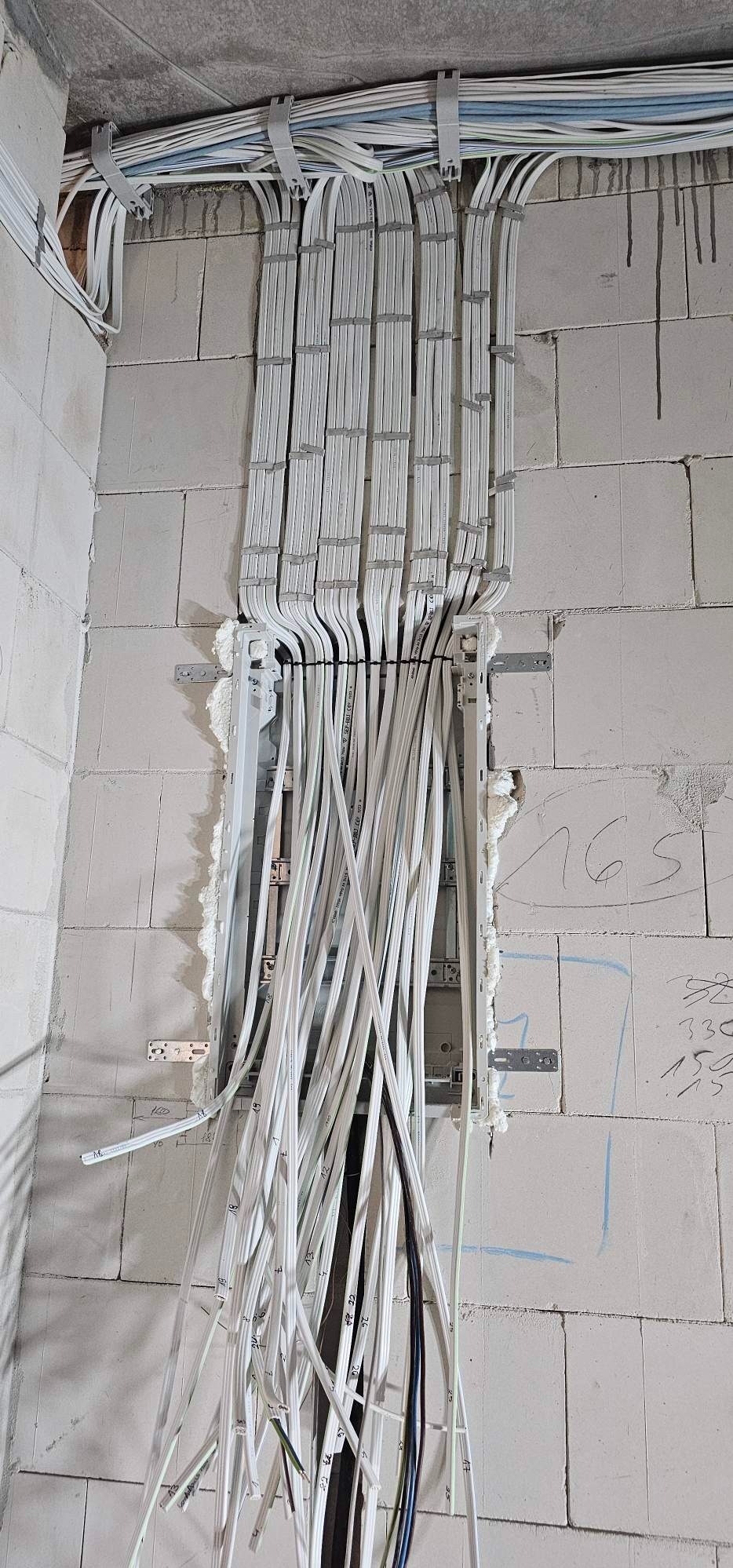 Pionowe ułożenie wiązki kabli elektrycznych w korycie w ścianie z betonu komórkowego, zabezpieczone pianką montażową.