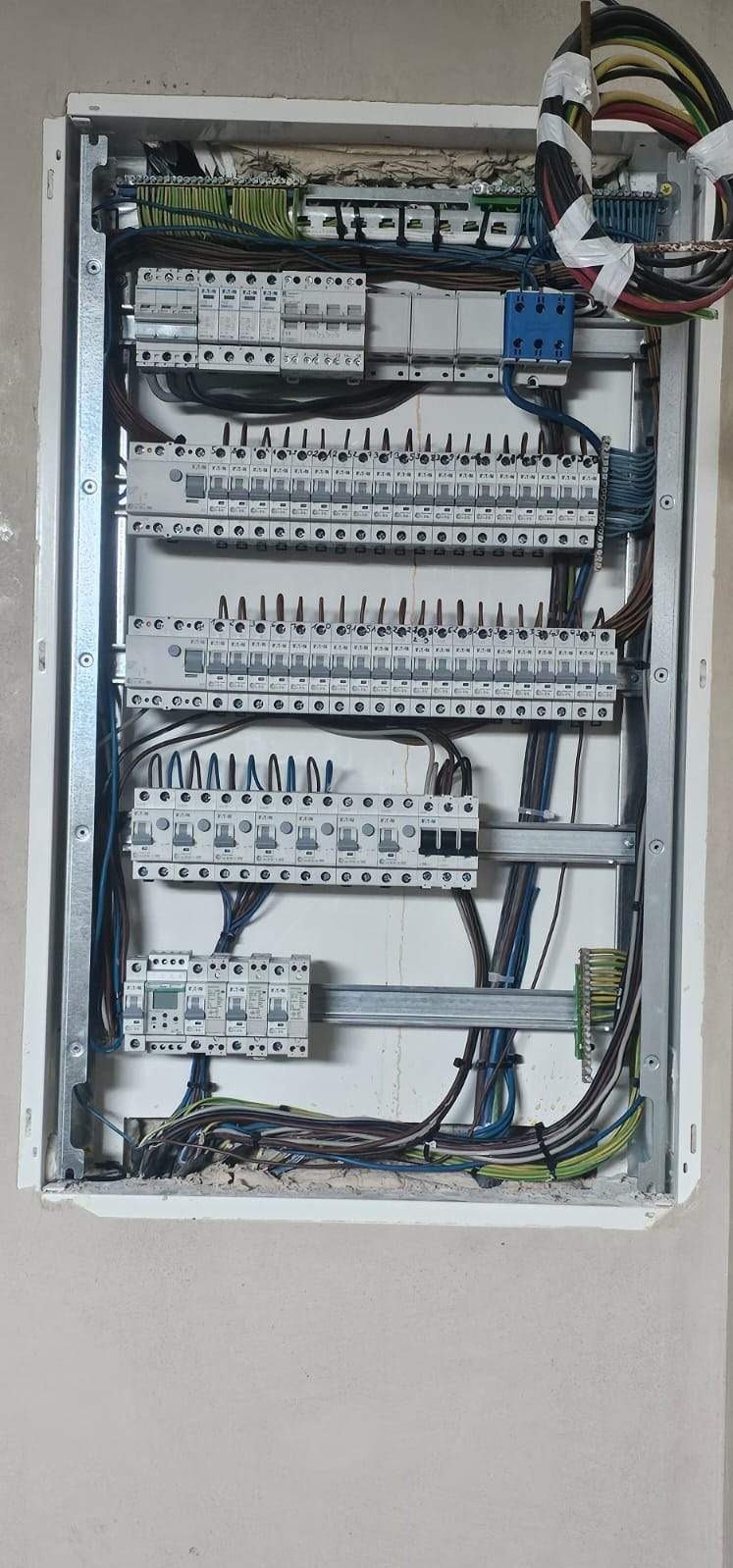 Otwarta skrzynka rozdzielcza z zamontowanymi bezpiecznikami i przewodami, widoczne połączenia elektryczne i kable w różnych kolorach.