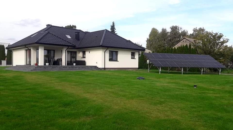 Instalacja fotowoltaiczna na trawniku obok domu jednorodzinnego we Wrocławiu. Panele słoneczne ustawione na metalowej konstrukcji, widoczne z daleka na tle zielonej trawy i budynku.