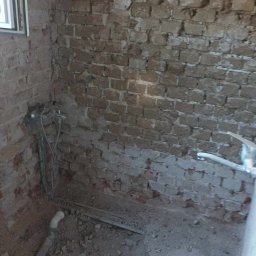 Marek Turowski Usługi Ogólnobudowlane - Zdjęcie łazienki w trakcie demontażu, widoczne odsłonięte cegły, stare rury i gruz na podłodze, z napisem 'PRZED' w dolnej części kadru.