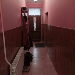 Marek Turowski Usługi Ogólnobudowlane - Korytarz w odcieniach różu i brązu przed remontem, widoczne boazerie, płytki podłogowe i grzejnik.