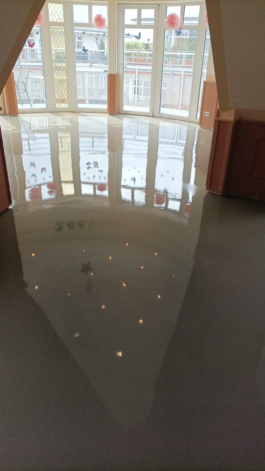 Błyszcząca, szara podłoga z efektem gwiazd w pokoju z dużymi oknami w Wolinie. Widoczne refleksy światła na gładkiej powierzchni.