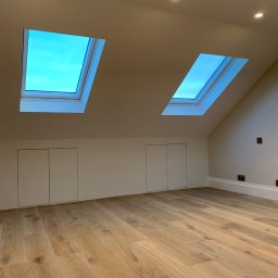 Mike. Elita w branży remontowej - Jasne, przestronne poddasze z drewnianą podłogą, dwoma oknami dachowymi z widokiem na niebo, wbudowanymi szafkami i punktowym oświetleniem.