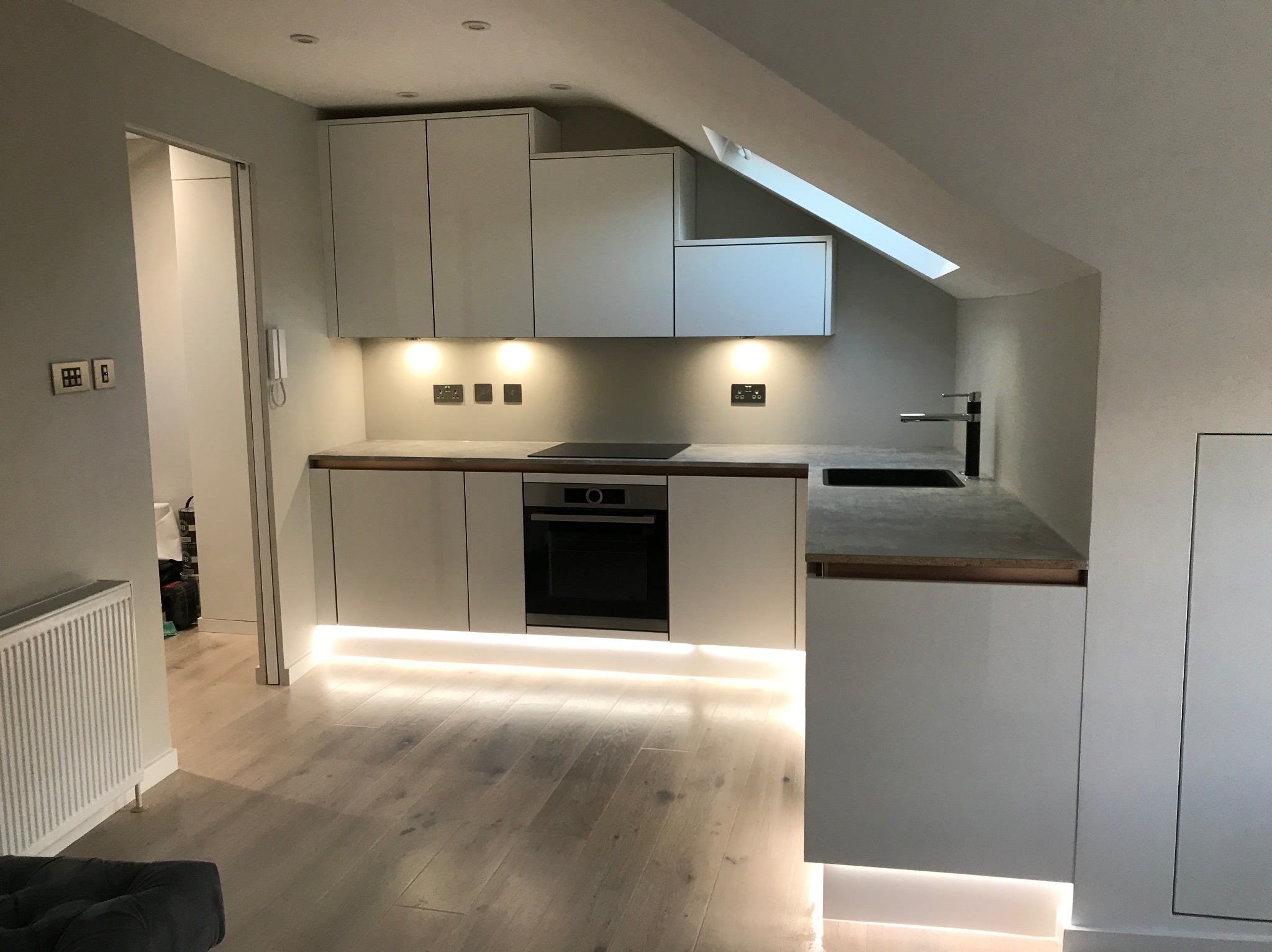 Nowoczesna, jasna kuchnia na poddaszu ze skośnym oknem dachowym, oświetleniem LED pod szafkami i drewnianą podłogą.