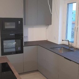 Rad Meble Piotr Radzioch - Szara, nowoczesna kuchnia z blatem imitującym marmur, wbudowanym piekarnikiem i mikrofalówką, oraz niedokończonymi kablami wychodzącymi ze ściany.