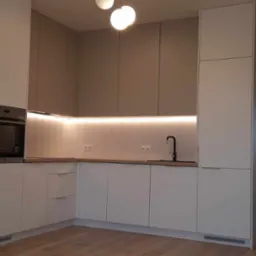 Nowoczesna kuchnia na wymiar w odcieniach bieli i szarości z podświetleniem LED pod szafkami wiszącymi, czarna bateria kuchenna i widok na korytarz.