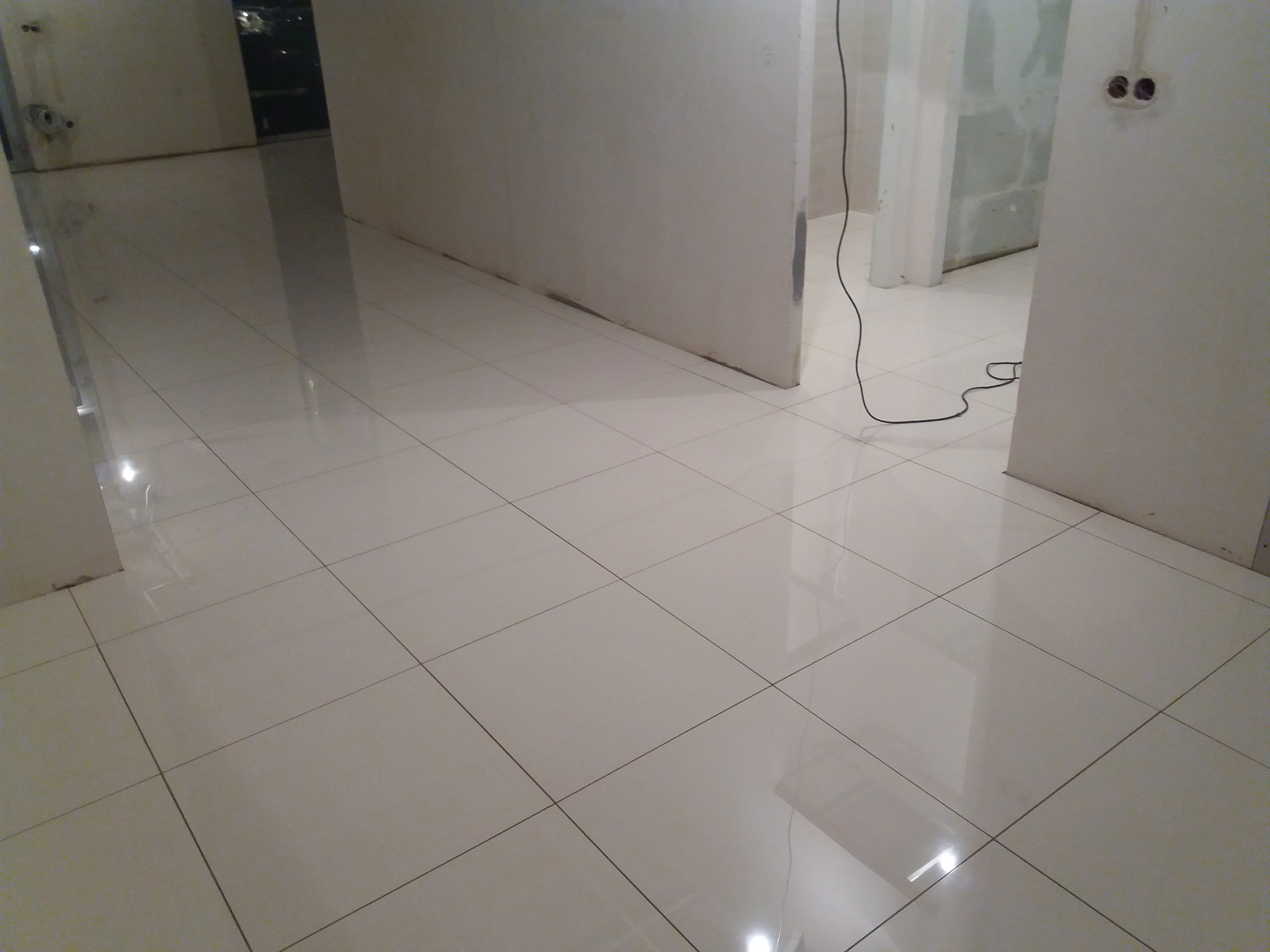 Błyszcząca, kremowa podłoga z płytek ceramicznych w trakcie remontu, widoczne surowe ściany i wystające kable elektryczne.