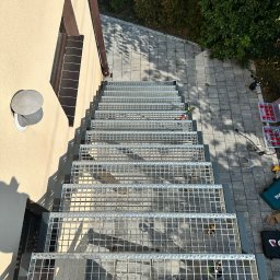 Mateusz Raniewicz - Zewnętrzne kratowe schody z metalu, widok z góry podczas montażu, narzędzia i skrzynki z elementami montażowymi obok, kostka brukowa na podłożu.