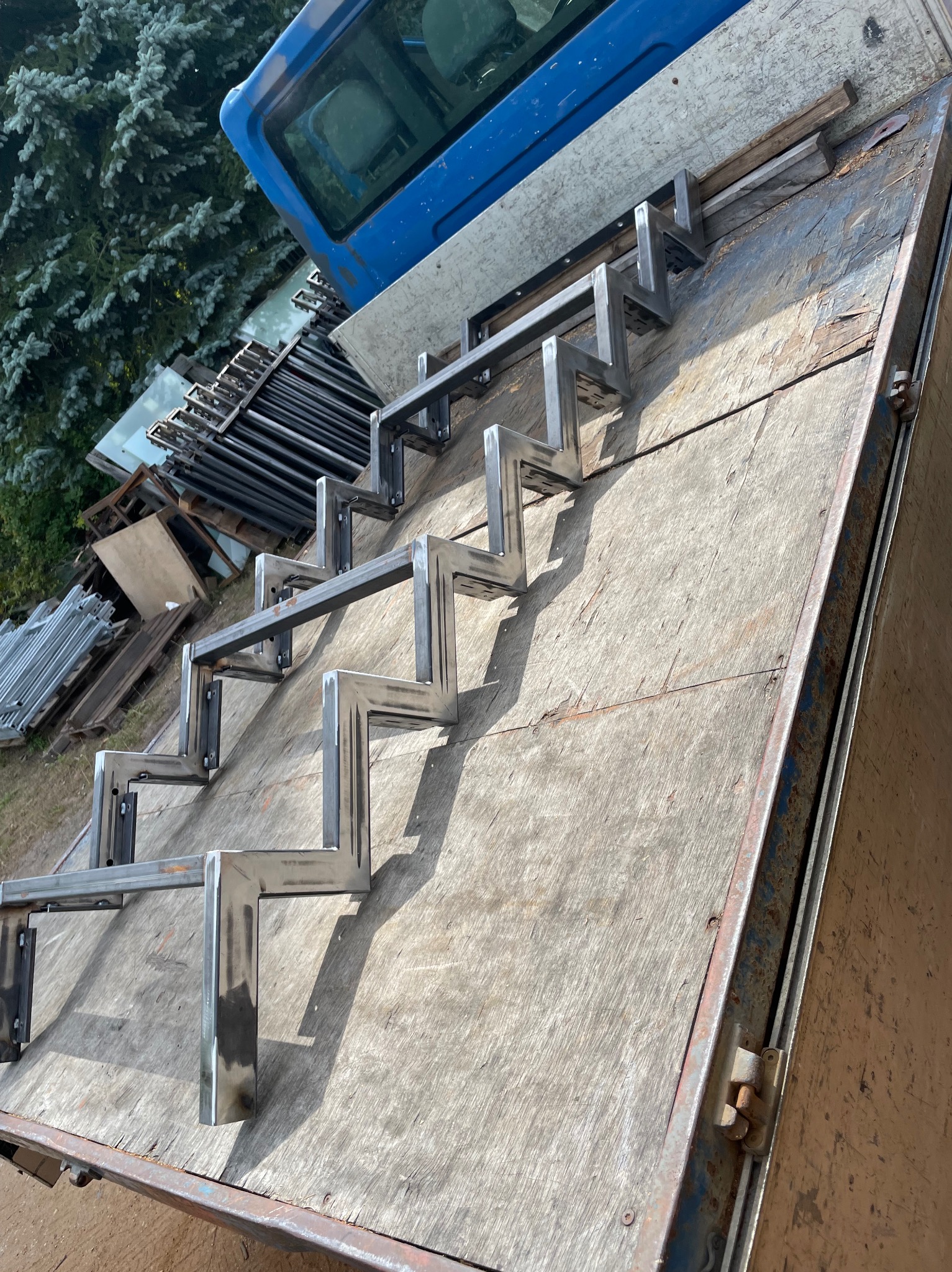 Surowe, metalowe stopnie schodowe, wstępnie pospawane, leżące na pace samochodu dostawczego, gotowe do transportu.