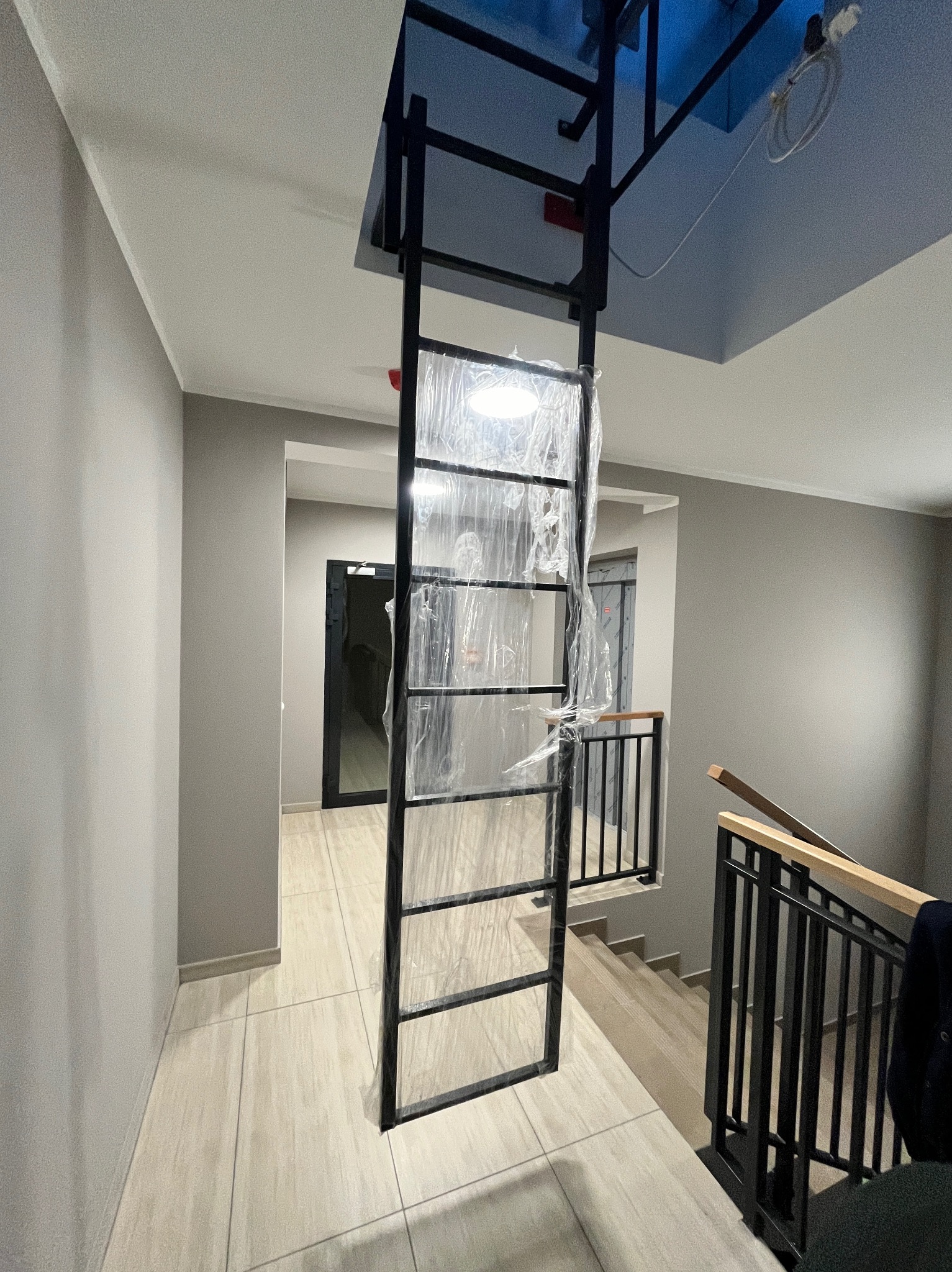 Wewnętrzna klatka schodowa z metalową konstrukcją schodów w trakcie montażu, zabezpieczona folią ochronną, widok na schody i balustradę w tle.