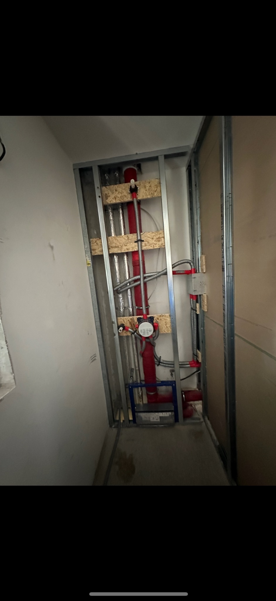 Wewnętrzna instalacja wodna i grzewcza w trakcie montażu, widoczne rury w izolacji, metalowa konstrukcja szkieletowa ścian działowych i elementy mocujące.