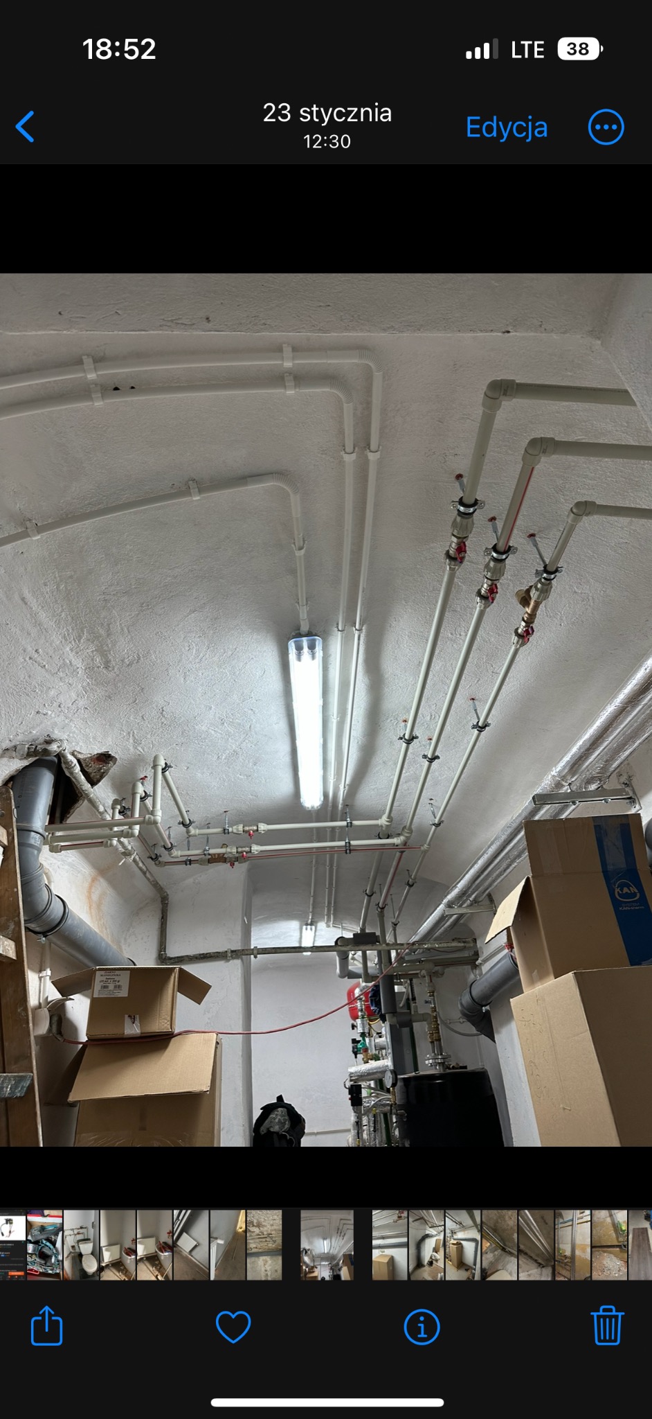 Rozbudowana instalacja rur pod sufitem piwnicy z widocznym zbiornikiem i licznymi zaworami, oświetlona jarzeniówką.