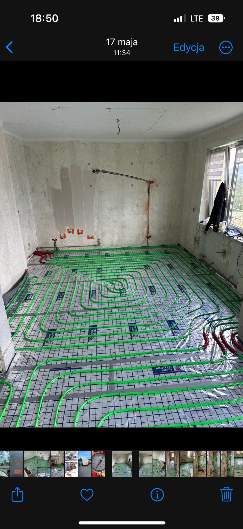 Wnętrze w trakcie montażu ogrzewania podłogowego: zielone rurki ułożone na folii z siatką, widoczne przyłącza do instalacji na ścianie w surowym stanie.