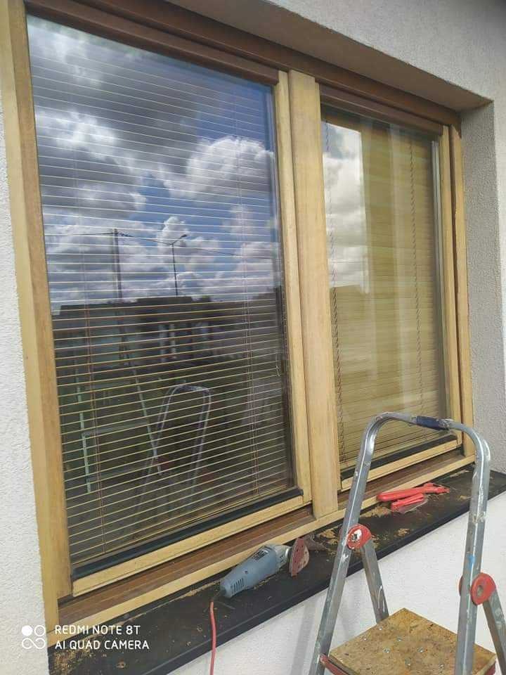 Drewniane okno z żaluzjami w trakcie prac, widoczna szlifierka kątowa na parapecie i drabina.