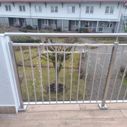 M-J-Stal Grzegorz Molenda - Balkon z prostą, metalową balustradą z pionowych prętów, widok na dziedziniec z drzewem ozdobionym lampkami, budynek z gabinetami lekarskimi w tle.