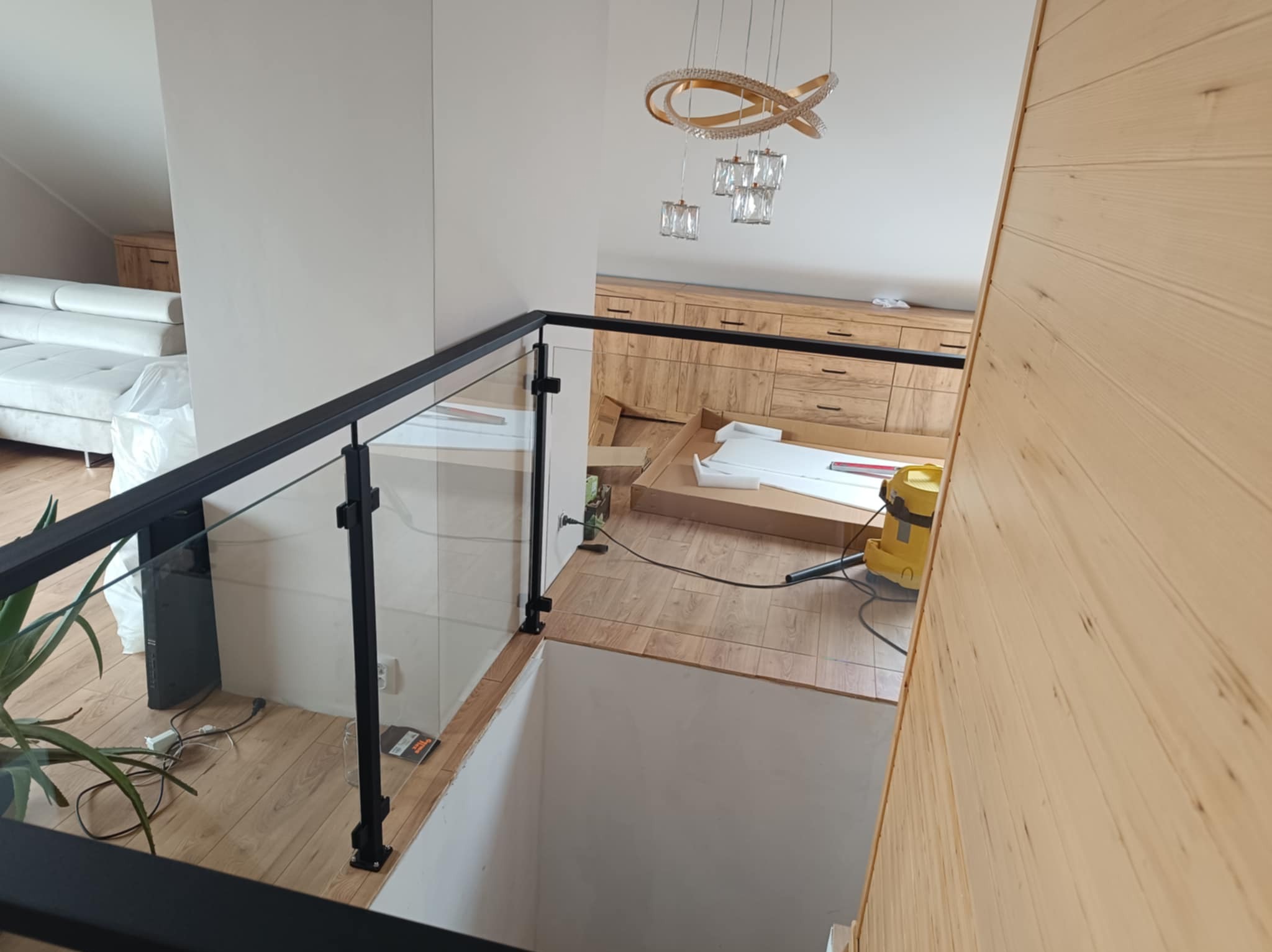 Nowoczesna balustrada szklana z czarnymi słupkami, widok z góry na jasne wnętrze z drewnianymi elementami i ozdobnym oświetleniem. Nowoczesny design.