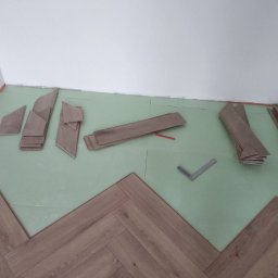 VVB group PL - Fragment podłogi w trakcie montażu z ułożonym wzorem w jodełkę; widoczne docięte panele, zielona podkładka i kątownik.