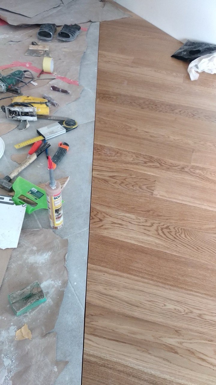 Fragment podłogi z ułożonym parkietem dębowym, widoczne narzędzia pracy, klej do parkietu i fragment podłoża przygotowywanego do dalszego układania.