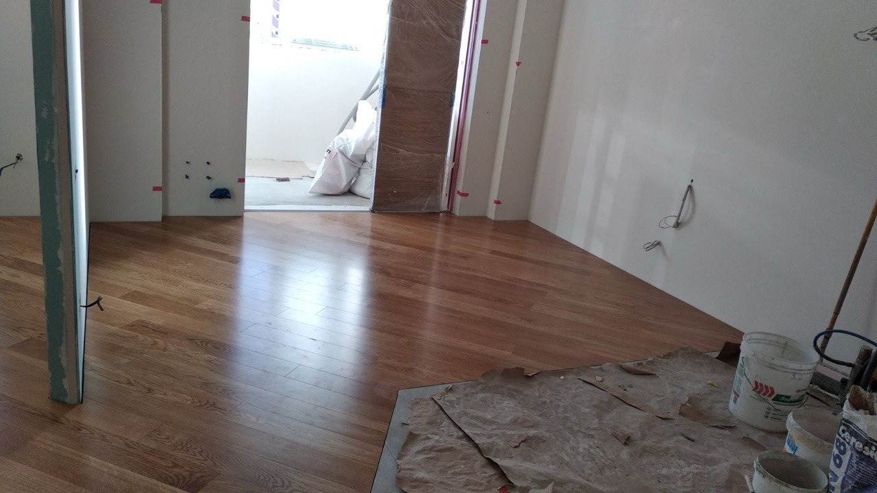 Wnętrze w trakcie prac wykończeniowych: ułożona drewniana podłoga z widocznymi pozostałościami po pracach malarskich i wiaderkami z farbą, ściany przygotowane do malowania, odkryte instalacje...