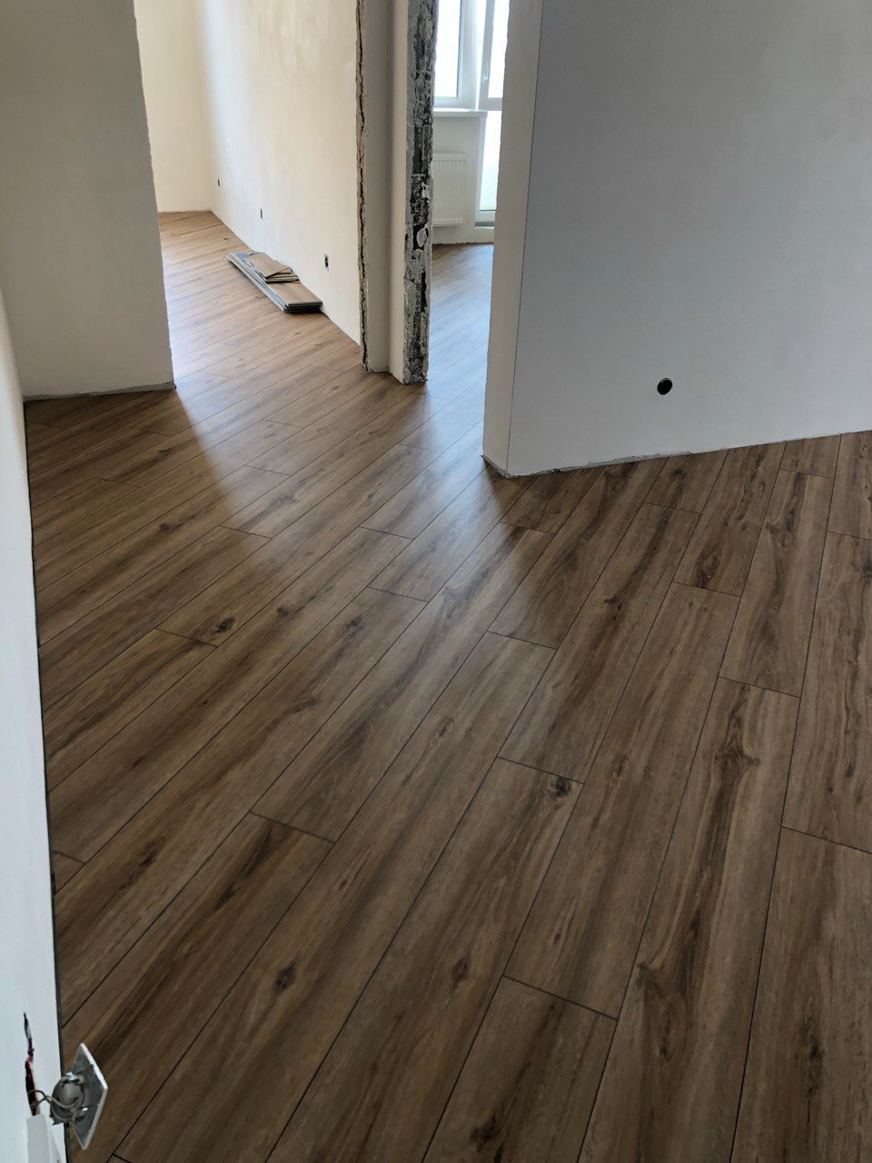 Ułożona podłoga z paneli imitujących drewno w trakcie remontu mieszkania, widoczne niedokończone ściany i przygotowane panele w tle.