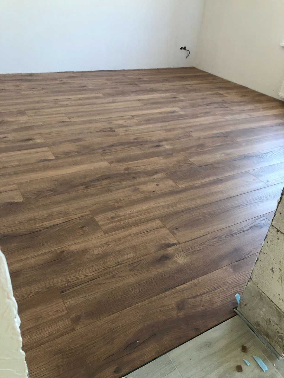 Nowo ułożona podłoga z paneli imitujących drewno w pustym pomieszczeniu, widoczne niedokończone wykończenie przy ścianie.