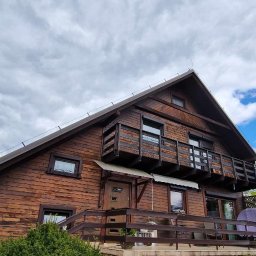 Haratyk - Dwupiętrowy dom z bali z dwoma balkonami, widok z dołu na tle pochmurnego nieba.